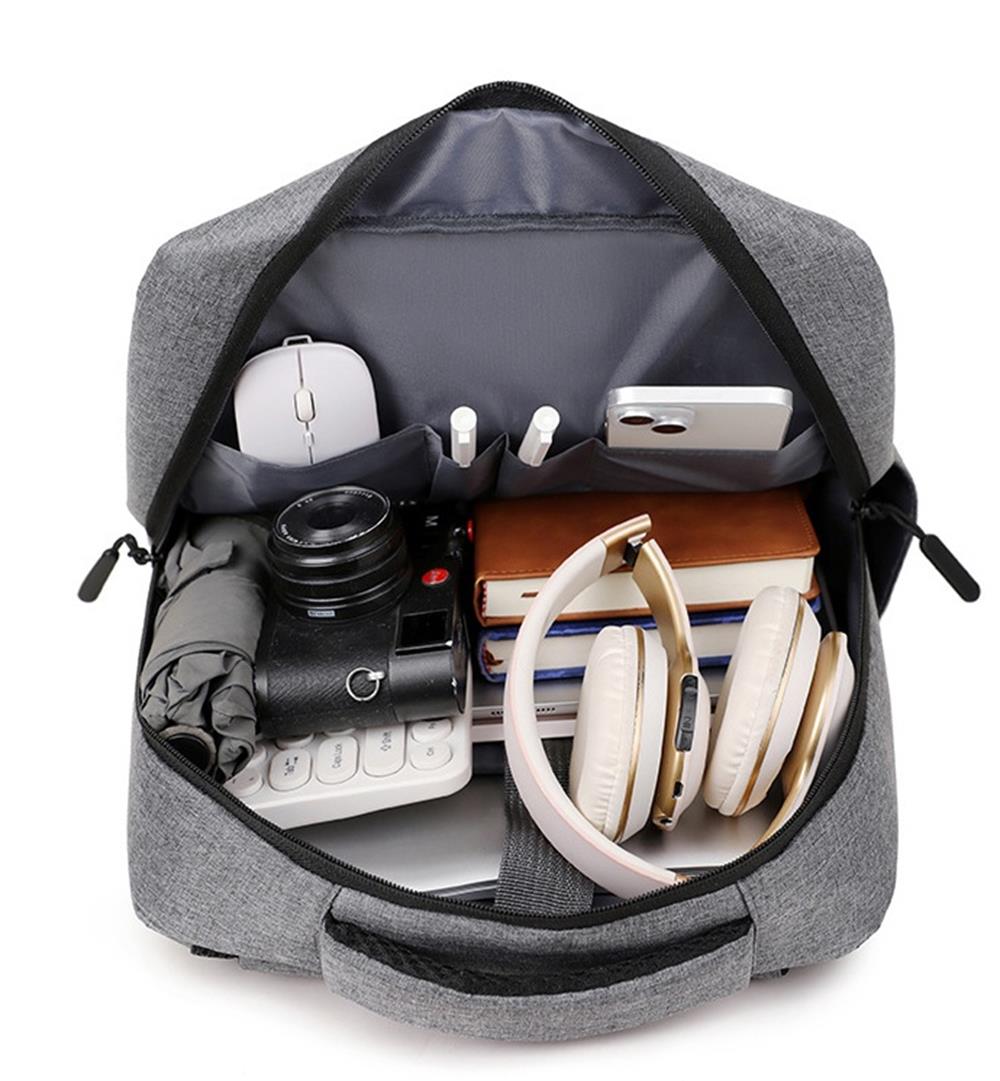 Same grey backpack fully opened flat from above showing back-panel slip pockets, a padded sleeve with a retention strap across the centre, and office gadgets packed as sizing props