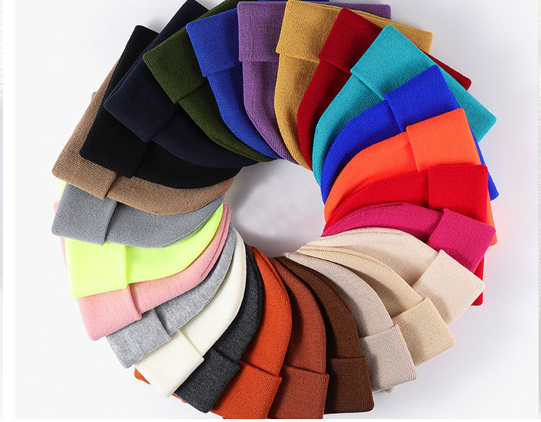 two dozen solid-colour cuffed rib-knit beanies arranged in a radial colour wheel on white