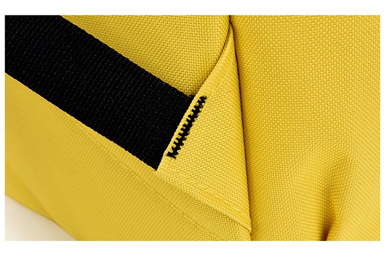 Close-up of a sunflower-yellow backpack panel where a black ribbed webbing strap is anchored, the joint reinforced with a diagonal line of black bar-tack stitching