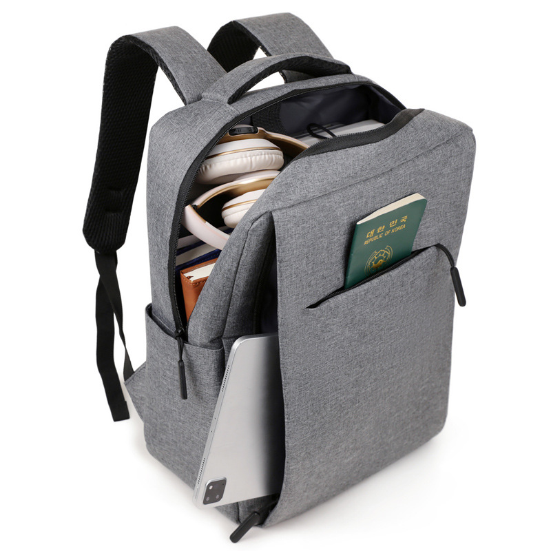 Rear three-quarter view of the grey backpack with the main zip open, black air-mesh lined padded shoulder straps, fabric-wrapped grab handle, zip side pocket holding a flat tablet-shaped prop and a booklet prop in the front slip pocket