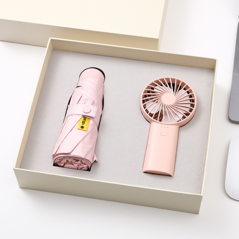 Blush pink folding umbrella and matching handheld fan packed side by side in a cream rigid gift box with grey insert