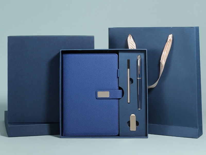 Navy executive set staged with standing lid and matching paper gift bag with champagne satin ribbon handles; cobalt textured journal with blank silver plate, navy pen, silver stylus and polished metal USB bar in the fitted navy insert